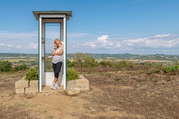 A woman talks on the phone in a telephone booth located in a secluded countryside area, Santo...