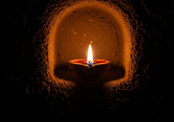 One small diwali diya flickering flame oil lamp are arranged in a square layout. The lamp set in a textured clay background.