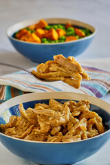 simmered chicken thighs in brown gravy served with steamed carrots and peas