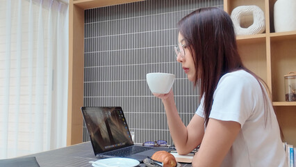 A woman is sitting at a desk with a laptop and a white bowl of food