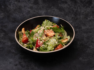 A vibrant and colorful salad mix that includes fresh greens, ripe tomatoes, crunchy cashews, and sesame seeds in black bowl on blackboard.