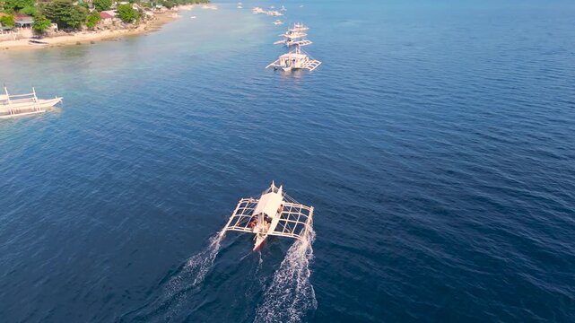 Aerial of several traditional Filipino outrigger boats (bangkas) sailing on clear blue ocean water near the coast of Moalboal, Cebu, Philippines.