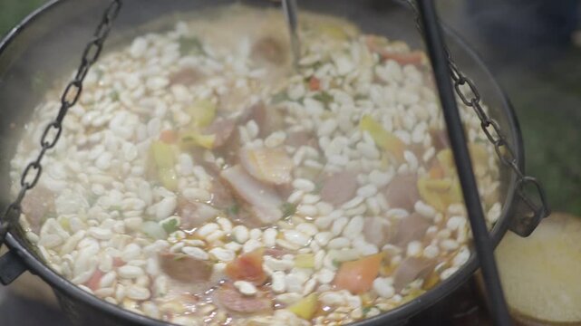 Chef using a ladle to mix cooking beans ina  pot, outdoor food preparation, close up