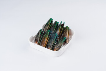 Close up view of several green and brown shellfish arranged in a white square container against a bright white background.