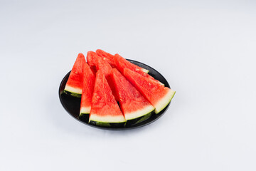 Slices of juicy red watermelon arranged on a small black plate against a bright white background.