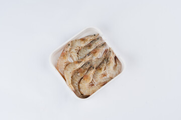 Overhead shot of seasoned shrimps in a square white container on a white background.