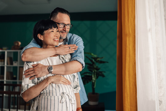 Happy pregnant interracial couple embracing at home