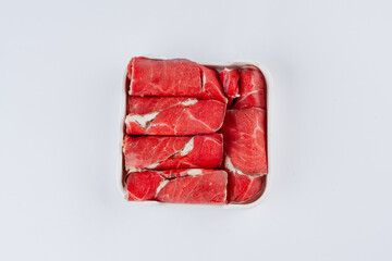 Overhead close up of thinly sliced raw red meat arranged neatly in a white square container against a white background.