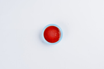 Overhead shot of a small light blue bowl filled with vibrant red sauce or jam against a white background.