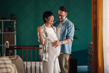 Happy couple expecting baby smiling and embracing in nursery