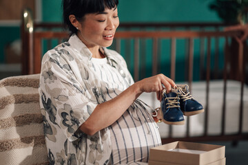 Pregnant woman holding baby shoes, getting ready for motherhood