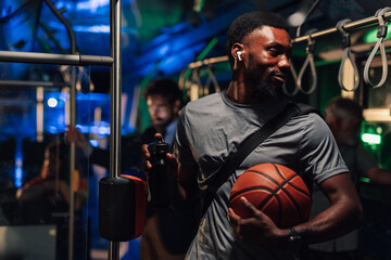 Young basketball player wearing wireless earbuds and holding ball on bus at night