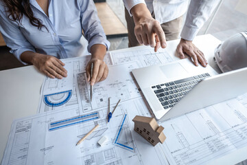 Team of architects or engineering consulting and analyzing working on objects tools and construction drawings inspection, discussing planning new architectural project on blueprint and model house