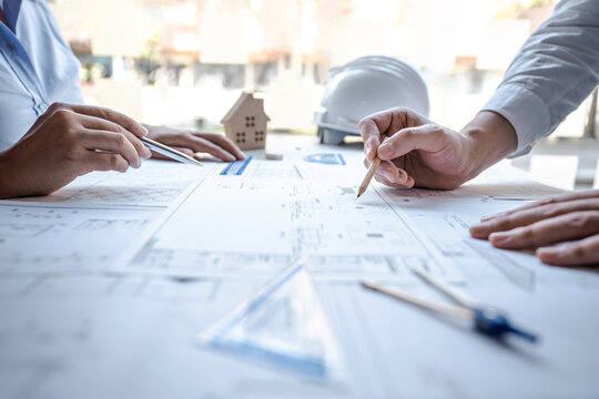 Team of architects or engineering consulting and analyzing working on objects tools and construction drawings inspection, discussing planning new architectural project on blueprint and model house