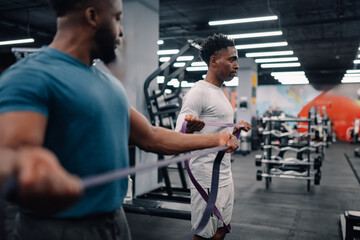 Two black men performing resistance band exercises in gym