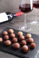 Tasty truffle bonbons and red wine on grey textured table, closeup