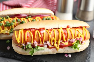 Delicious hot dogs with sauces, lettuce and onion on grey table, closeup