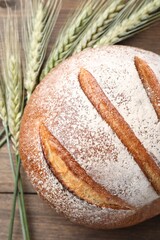 Fresh bread and green wheat spikes on wooden table, flat lay