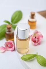 Bottles of cosmetic products, roses and basil on white table, closeup