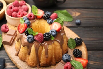 Tasty Bundt cake with berries, chocolate and mint on wooden table, closeup