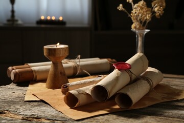 Old paper scrolls and burning candle on wooden table, closeup