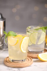 Tasty citrus cocktails in glasses on white marble table against blurred lights, closeup