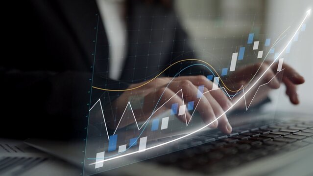 A close-up view of professional hands typing on a laptop, with digital graphs and charts symbolizing business growth, financial analysis, and strategic planning. Copula