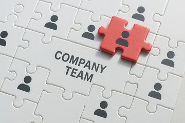 Company team concept with puzzle pieces showing human icons and one red piece symbolizing leadership or key member, representing collaboration and unity in business