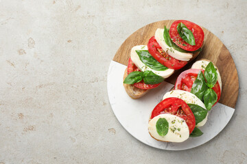 Delicious sandwiches with mozzarella cheese, tomatoes and basil on light grey textured table, top view. Space for text