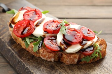 Delicious sandwich with mozzarella cheese, balsamic sauce, tomatoes and arugula on wooden table, closeup