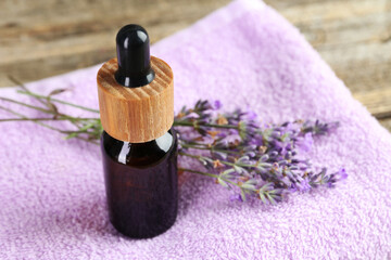 Lavender essential oil, flowers and towel on wooden table, closeup