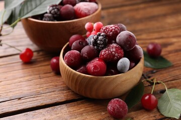 Mix of ripe frozen berries and green leaves on wooden table, closeup