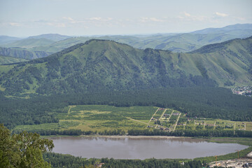 Obraz premium Scenic mountain landscape with forest, hills, and serene river in summer's lush green countryside.