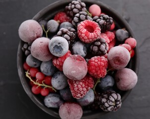 Mix of ripe frozen berries in bowl on dark textured table, top view