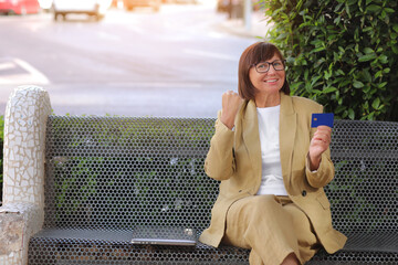 Happy joyful smiling freelancer adult woman 50-60 s wearing stylish suit is holding credit card she...