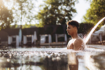 Young man relaxing in luxury hotel pool with cascading water feature