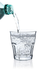 Pouring refreshing soda water from bottle into glass on white background