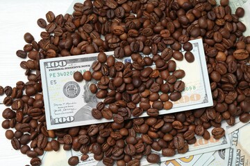 Pile of roasted coffee beans and dollar banknotes on white wooden table, flat lay