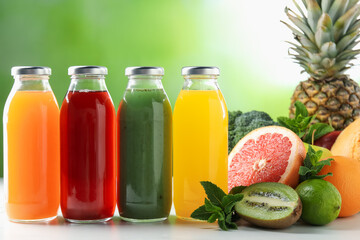 Tasty juices in glass bottles, fresh ingredients and mint on white table against blurred green background, closeup
