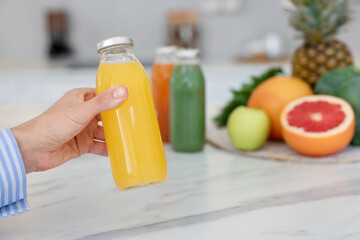 Woman with bottle of tasty juice at white marble table indoors, closeup