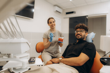 Fototapeta premium Dentist showing teeth model to patient in modern clinic