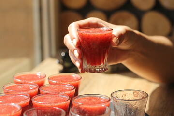 Hand holding small glass of fresh red smoothie. Healthy fruit drink served in multiple glasses on...