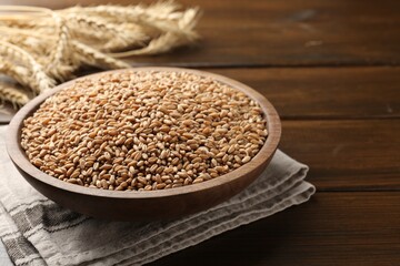 Wheat grains in bowl and spikelets on wooden table, closeup. Space for text