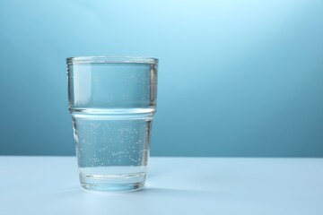 Refreshing soda water in glass on white table against light blue gradient background, closeup. Space for text
