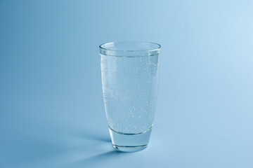 Refreshing soda water in glass on light blue gradient background, closeup