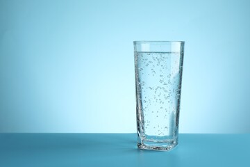 Refreshing soda water in glass on table against turquoise gradient background, closeup. Space for text