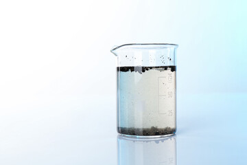 Glass beaker with dirty water on mirror surface, space for text