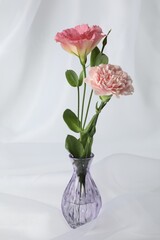 Beautiful flowers in glass vase on white cloth, closeup