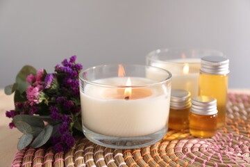 Burning candles, flowers and bottles of cosmetic products on table against grey background, closeup