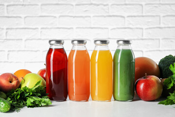 Tasty juices in glass bottles and ingredients on white table against brick wall